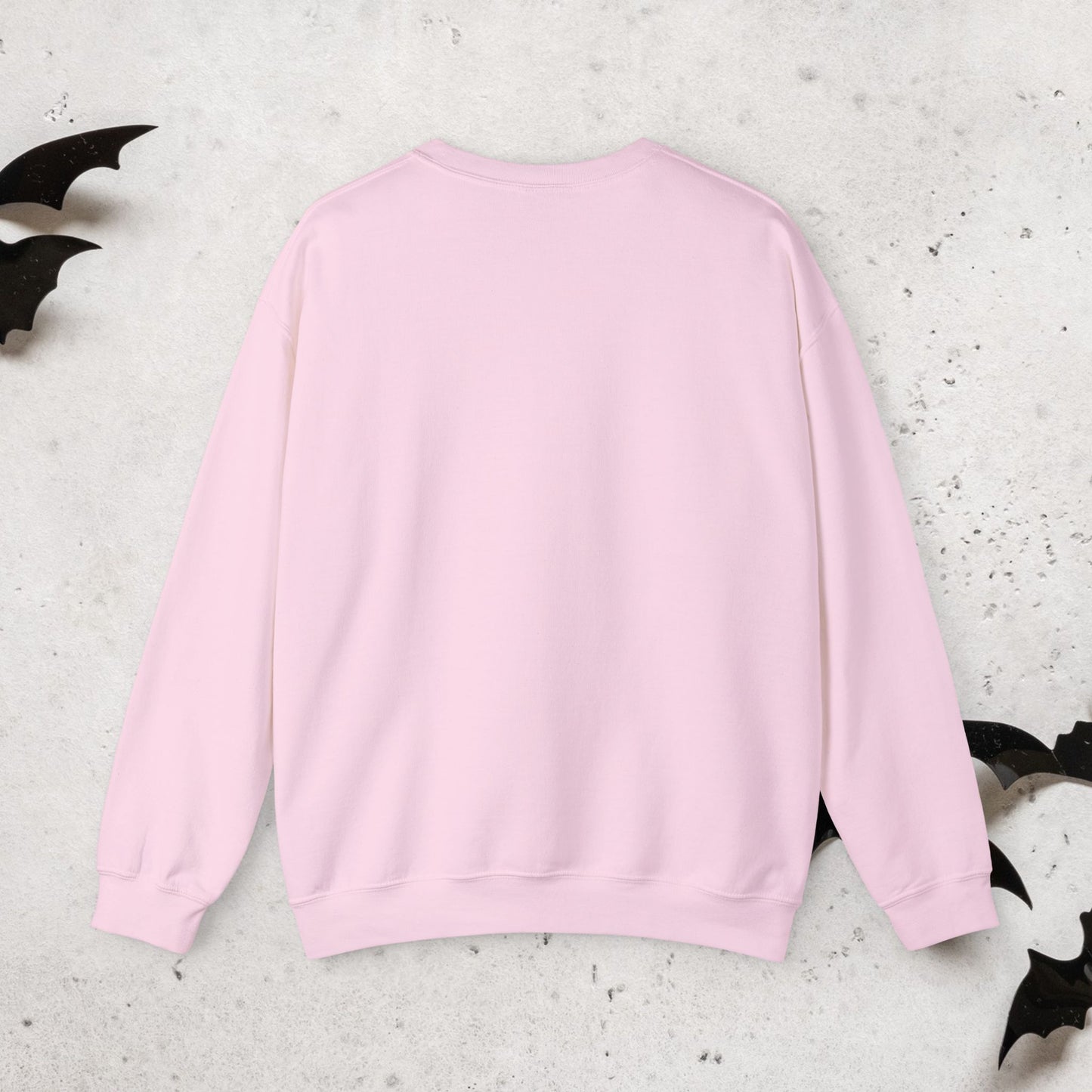 Pink sweatshirt on a textured white surface with black bat wings.