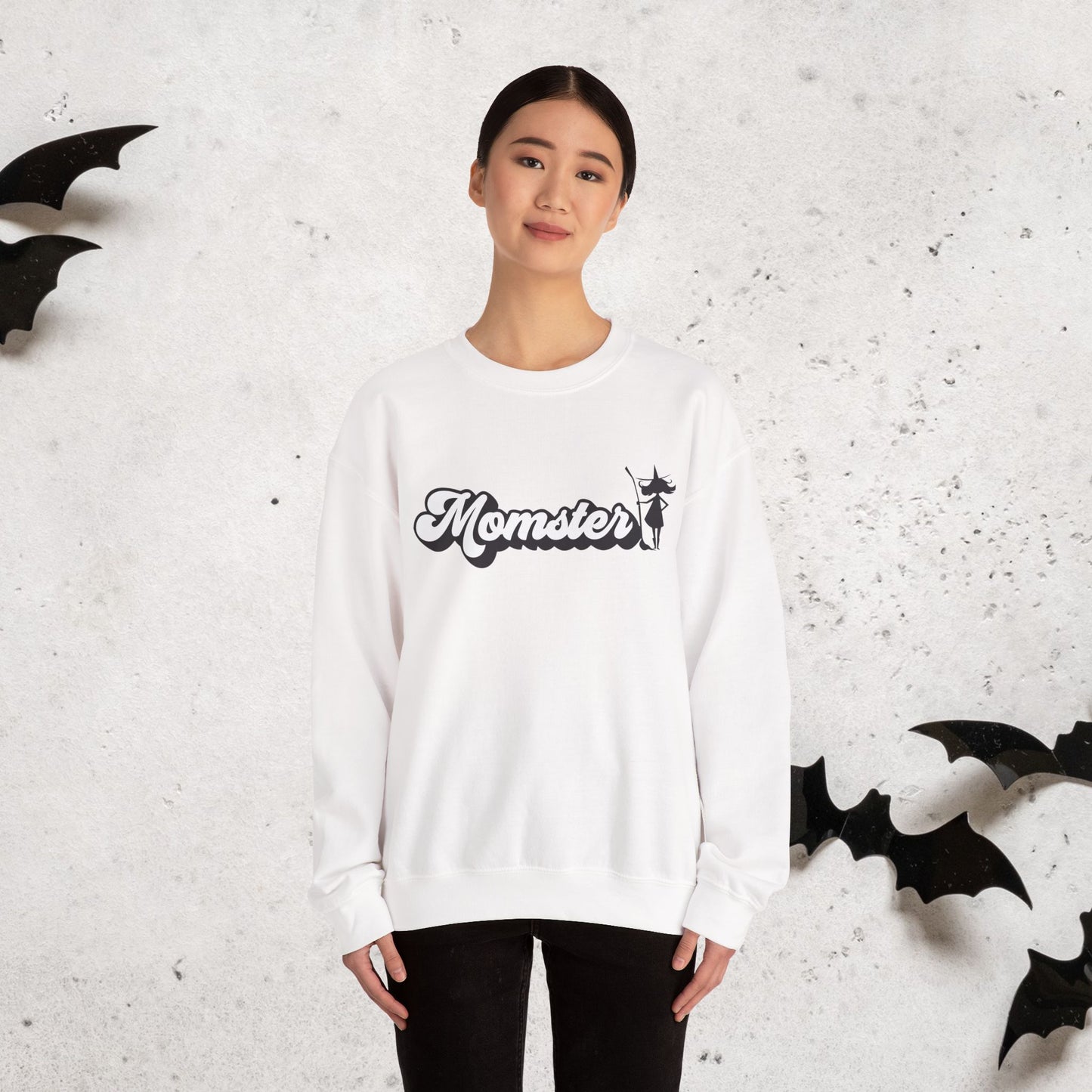 Person wearing a white halloween witch crewneck sweatshirt with 'Momster' text, surrounded by black bat shapes on a light gray background.