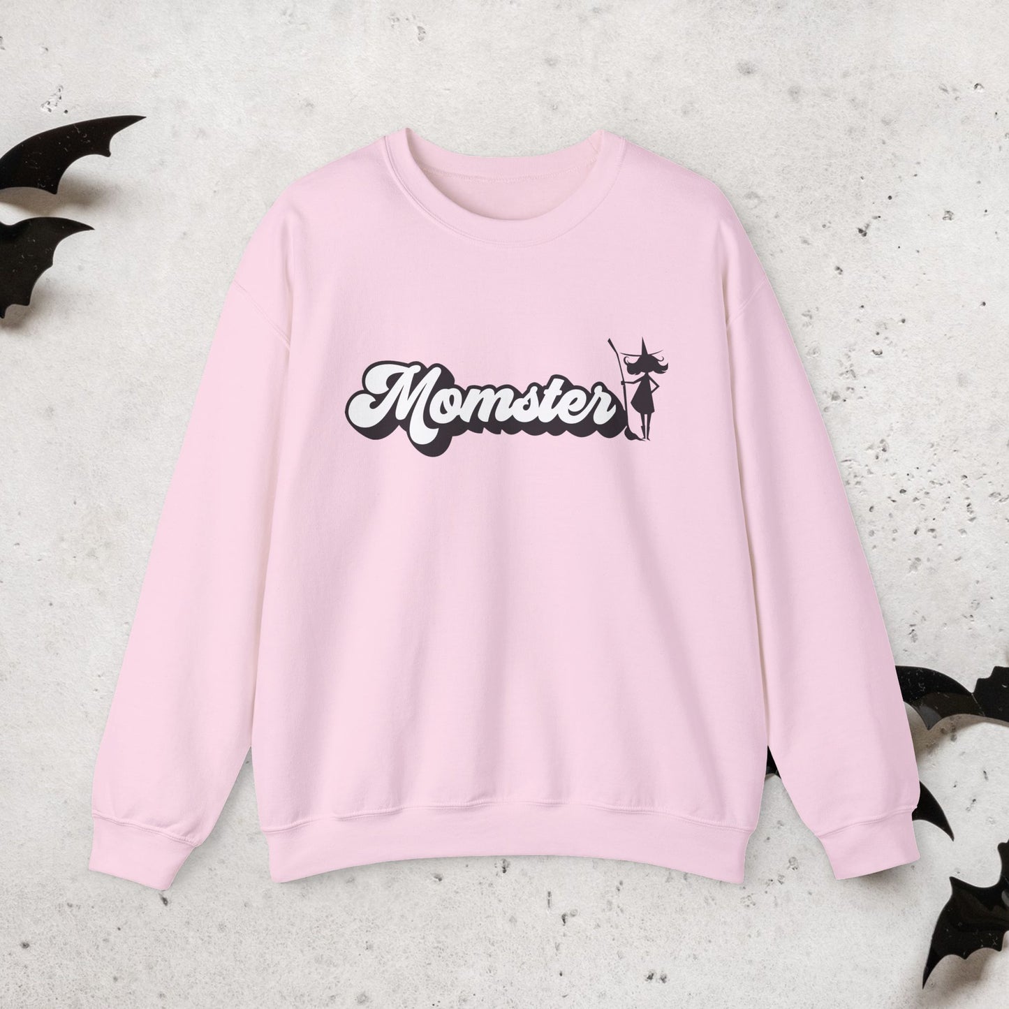 Pink sweatshirt with a Halloween witch 'Momster' design on a textured surface