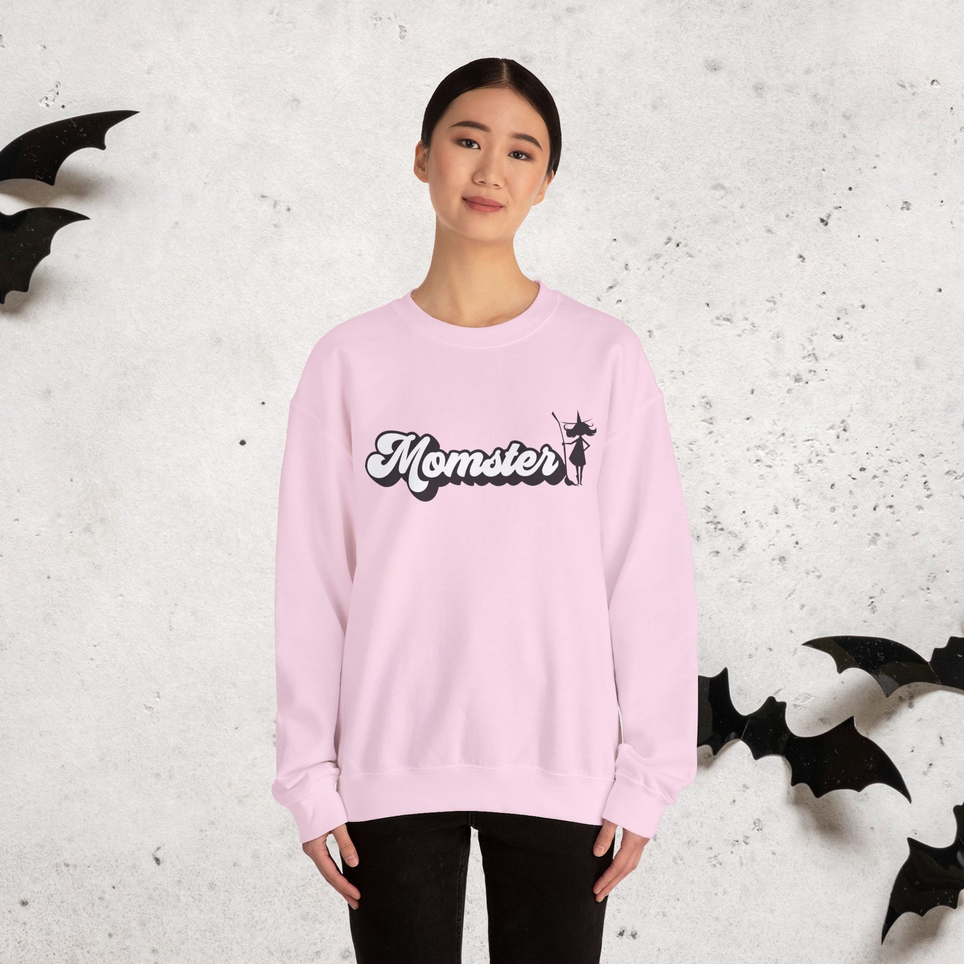 Person wearing a pink sweatshirt with 'Momster' text, standing against a textured white background with black bat decorations.