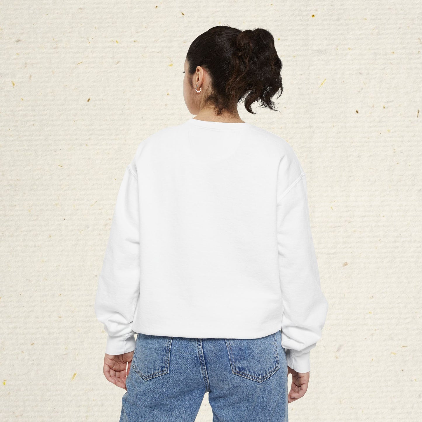 Person wearing a white sweatshirt and blue jeans against a textured beige wall