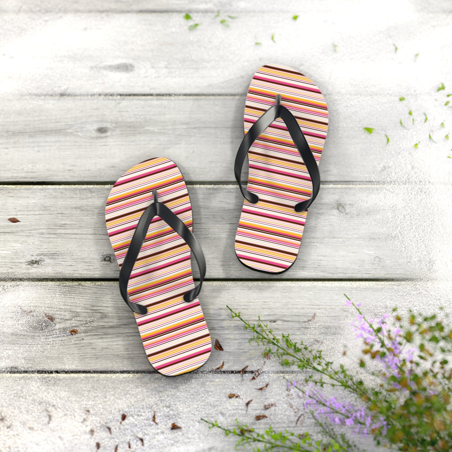 Pair of striped flip-flops on a wooden surface with flowers.