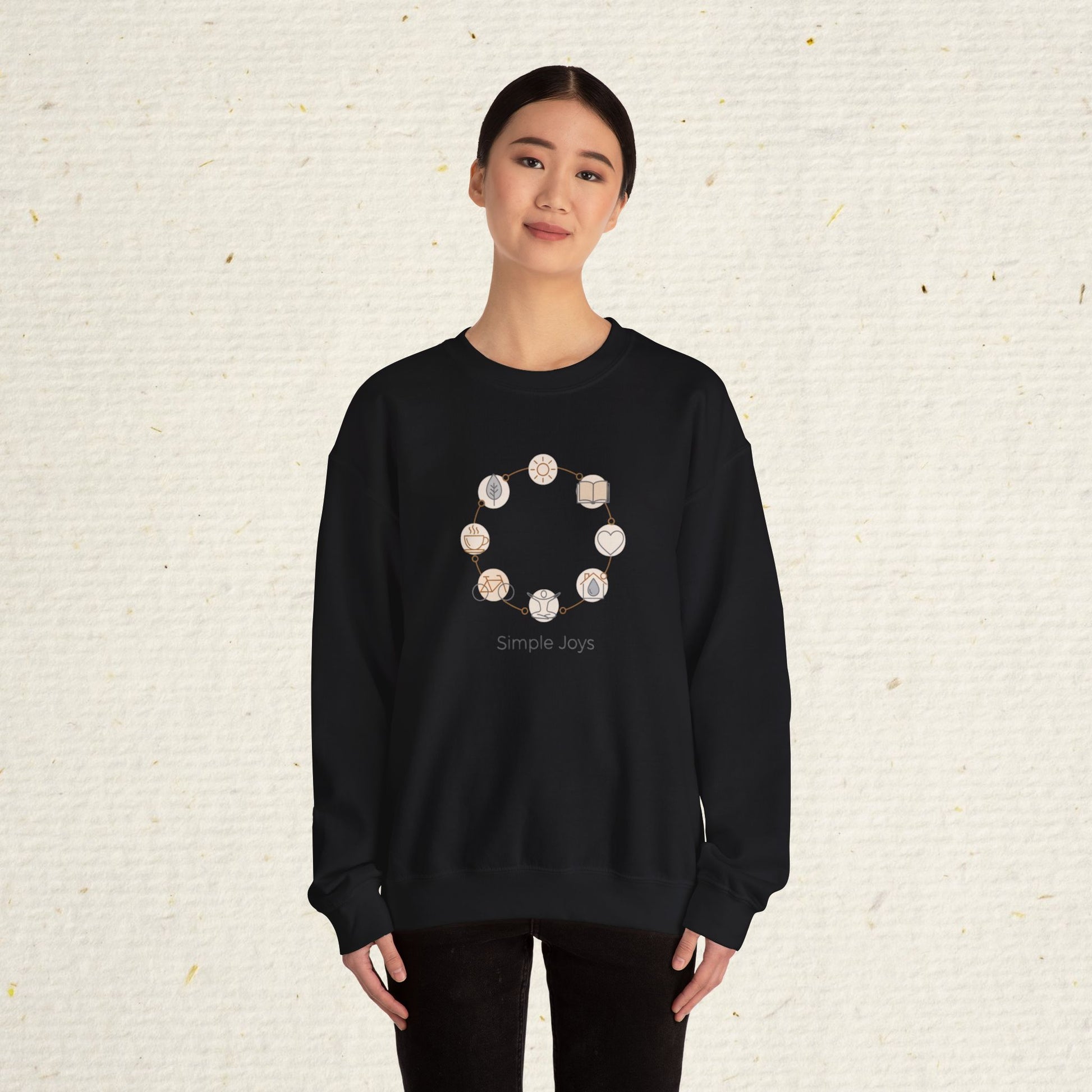 Person wearing a black sweatshirt with a circular design and 'Simple Joys' text on a textured beige background
