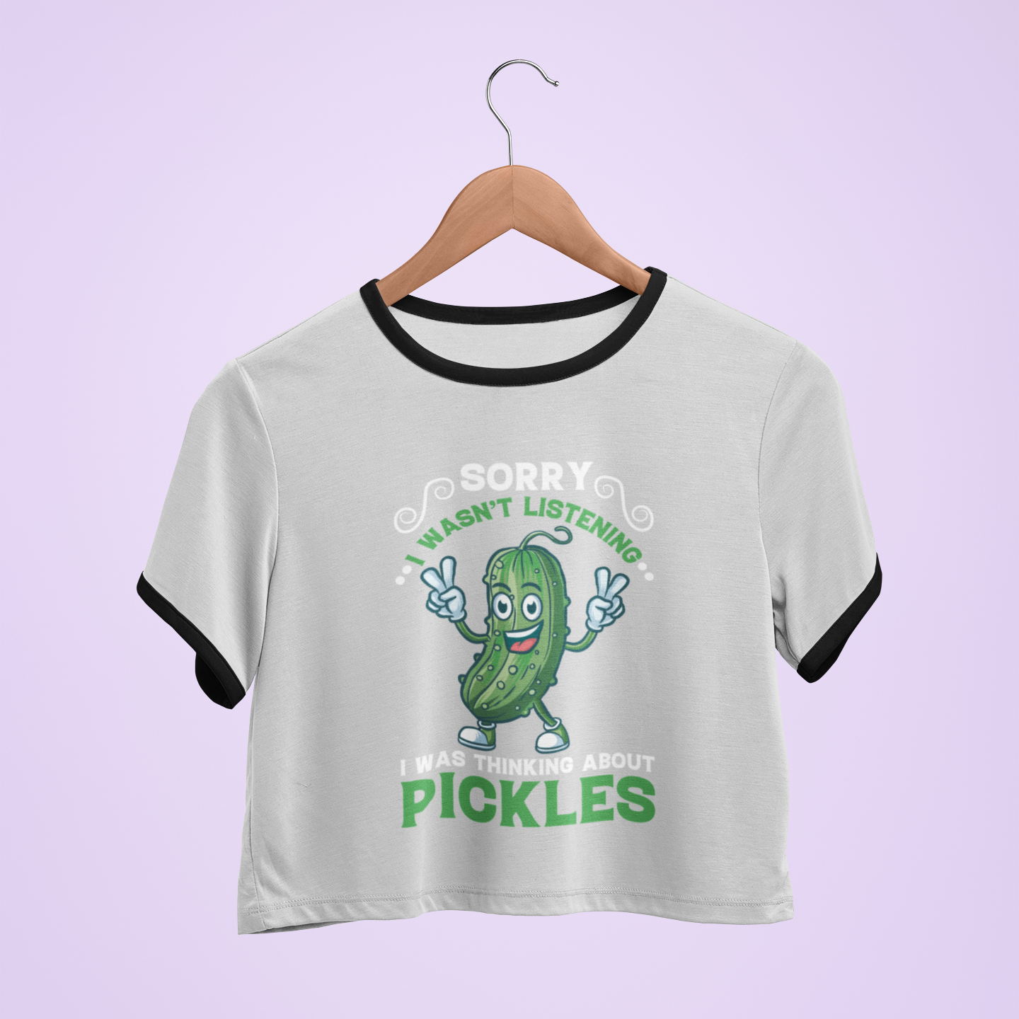 T-shirt with a pickle graphic and text on a hanger against a light purple background