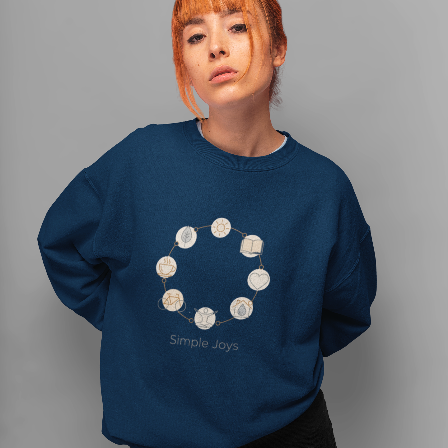 Person wearing a navy blue sweatshirt with 'Simple Joys' design on a gray background